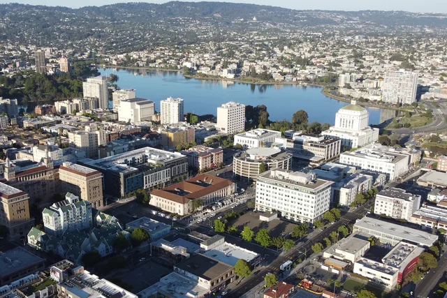 Lake Merritt viewed from downtown Oakland on a sunny afternoon. The shadows of downtown high-rise buildings cast over lower buildings just to the west of the lake. At the southern...