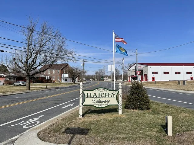 Sign for Hartly, Delaware and flagpole at the intersection of Delaware Route 11 (Arthursville Road) and Delaware Route 44 (Everetts Corner Road/Main Street)
