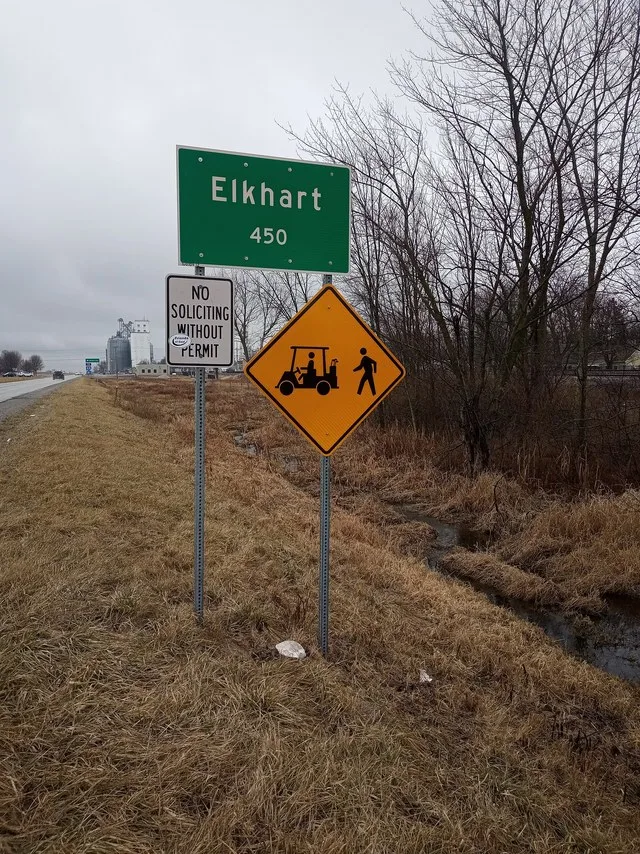 Sign at southern border of Elkhart Illinois, announcing the town population and warning of golf cart and pedestrian traffic. Also featuring a "Friends of Coal" sticker, possibly u...