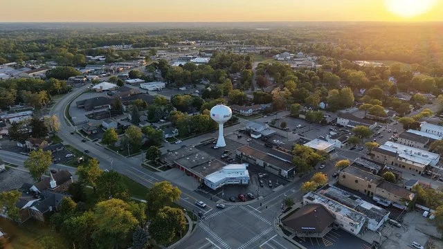 An aerial drone photograph of downtown Wauconda, Illinois, captured at sunset looking northwest. A white municipal water tower stands at the center, adjacent to the Wauconda Fire...