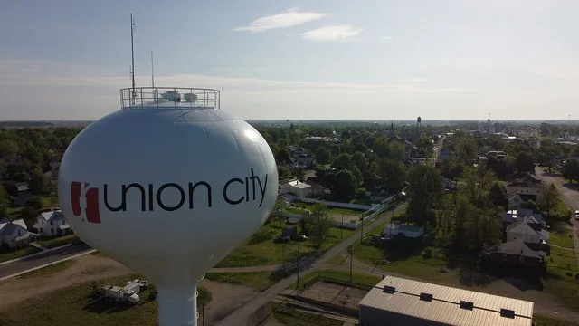 Drone shot looking past Union City, IN water tower to skyline