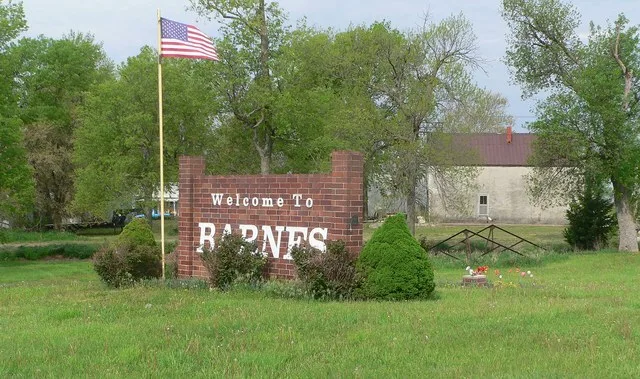 Welcome sign on south side of Kansas Highway 148 in Barnes, Kansas; seen from the east. Behind and to the right of the sign is the Washington County kingpost bridge, listed in the...