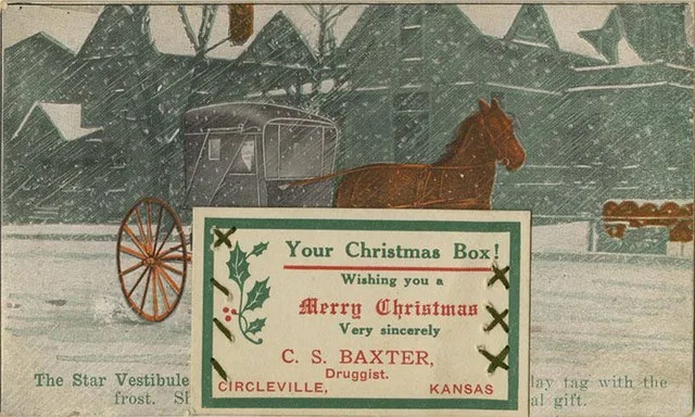 postcard of a horsedrawn wagon driving through a snow storm, attached is a sewn-on business card from C.S. Baxter Druggist