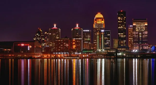 The skyline of Louisville, Kentucky, lit up at night, featuring the KFC Yum! Center and 400 West Market, among other buildings. Taken in 2021. Modified (cropped further from File...