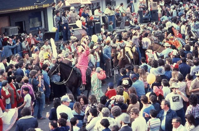 "Parade at Cajun Mardi Gras festival" 1989 Notes: Shows revelers, some riding horses, in traditional Cajun Mardi Gras outfits passing through crowds in front of Manuel's Bar, 6th...