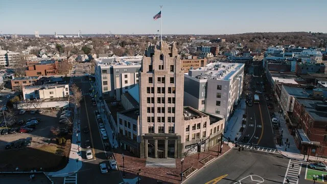 A drone shot of the Granite Trust Building in Quincy, MA. It shows the recently constructed apartments located behind it along with part of the new traffic pattern in the street i...