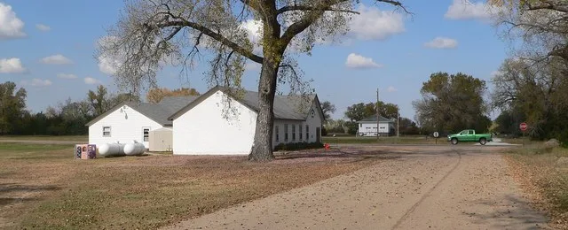 Burton, Nebraska ; seen from the south. In the foreground is the Assembly of God church; to its right, in the background, is Tall Tails Taxidermy. The green pickup is westbound on...