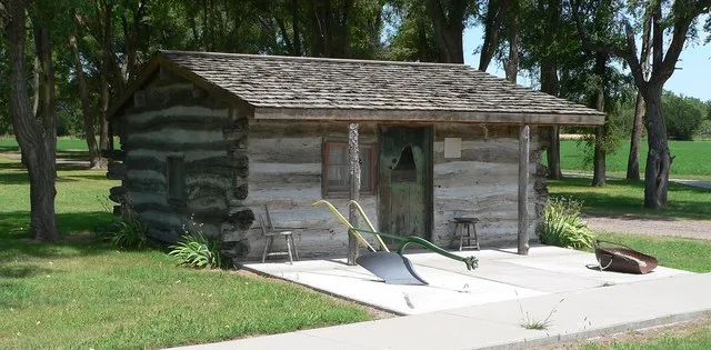 Log cabin in park in Holbrook, Nebraska ; seen from the southwest. A sign to the right of the door indicates that it was built in 1874.
