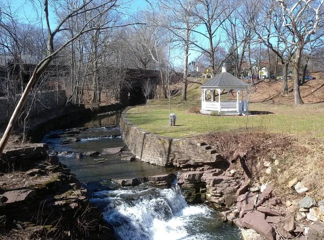 Looking north along Toney's Brook from footbridge at a gazebo on a former mill site on a sunny early afternoon.