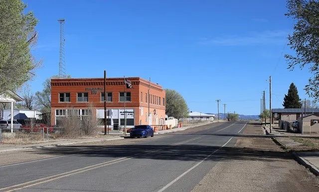 Looking north along 3rd Street in Maxwell, New Mexico . The red brick building on the left houses the town's post office. Lettering on the outside of the building says "Bank Build...