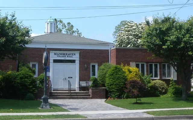 Looking north across Manorhaven Blvd at Village Hall on a mostly sunny midday.