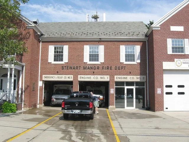 Looking east across Covert Avenue at en:Stewart Manor, New York firehouse (integrated with village hall) on a clearing early afternoon