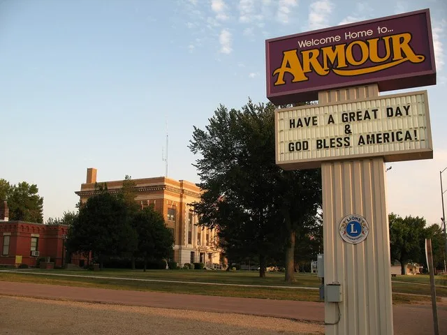 The town sign for Armour, South Dakota along Highway 281. The Douglas County Courthouse and Museum are visible in the background.