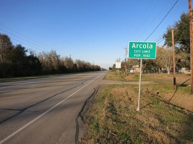 Photo shows the Arcola, Texas city limit sign on Farm to Market 521 between Glendale Lakes Drive and Sears Road. The view is looking north.