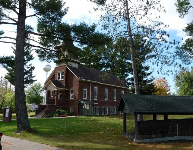 A scene from the village of Hawkins in north-central Wisconsin. Bethel Lutheran church is in the center. A historic pine log is on the right.