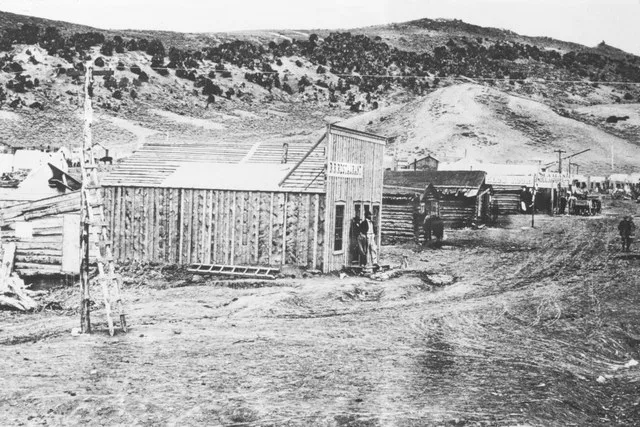 Two men stand outside a small wooden building with a sign that reads "R.R. Restaurant" in Bear River City, Wyoming. Original image and information can be found at the Wyoming Stat...